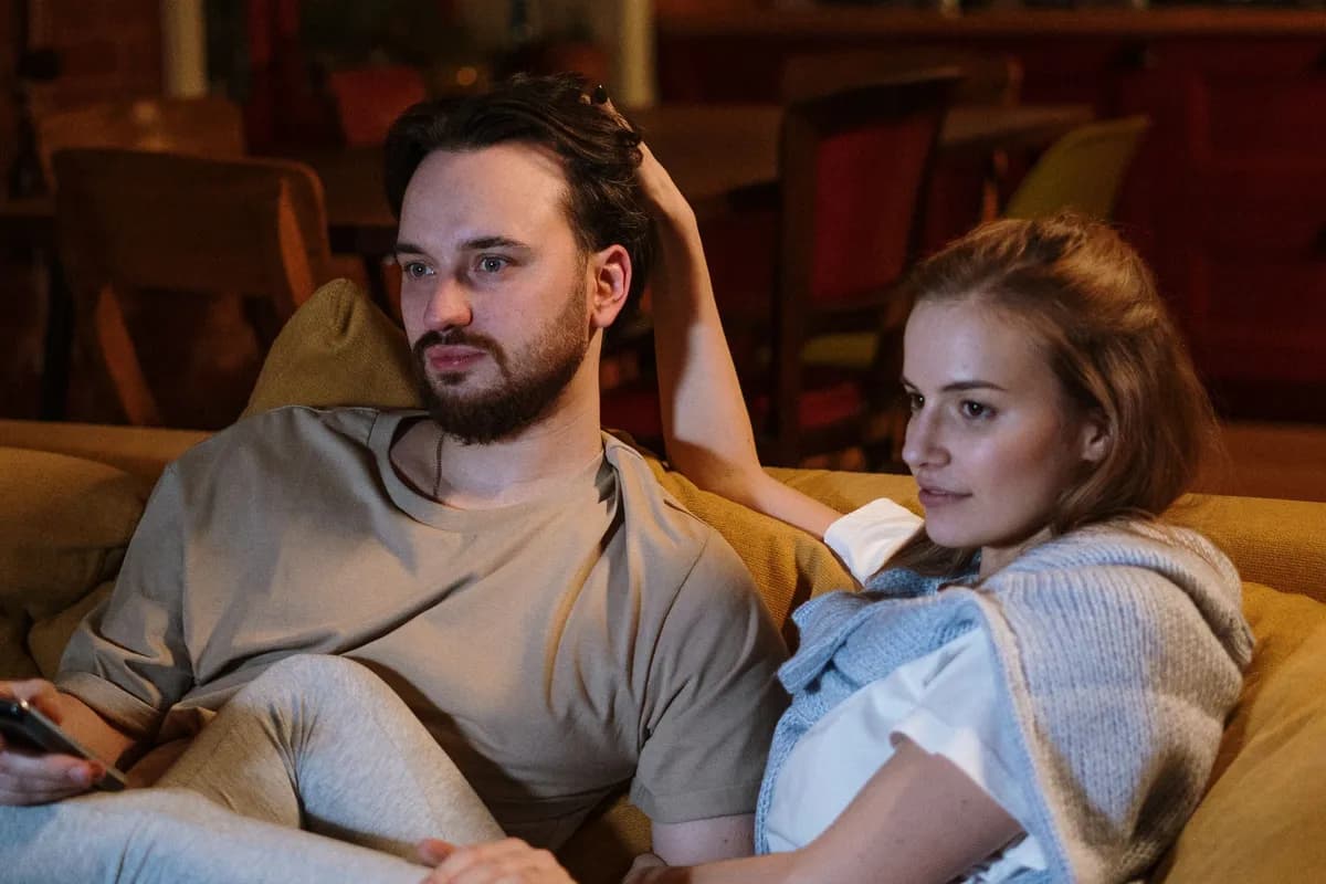 Paar entspannt abends auf dem Sofa beim Fernsehen, mit Fernbedienung in der Hand