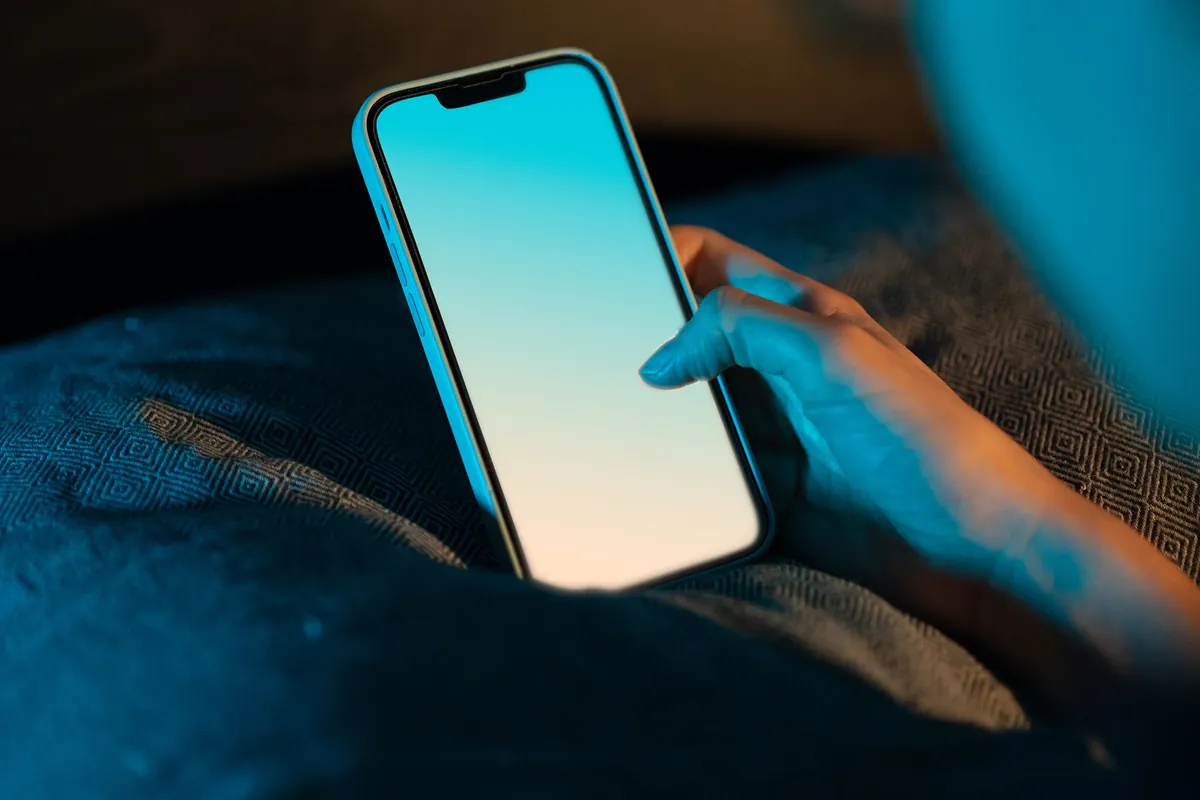 Hand hält ein Smartphone mit hellem Bildschirm über einer blauen Decke