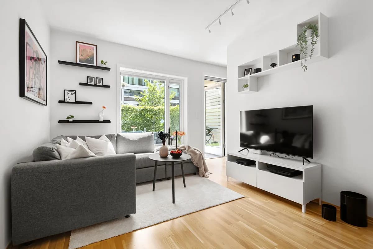 Helles Wohnzimmer mit grauem Sofa und Fernseher auf einem weißen Lowboard