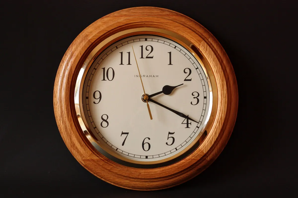 Runde Wanduhr mit Holzrahmen vor dunklem Hintergrund