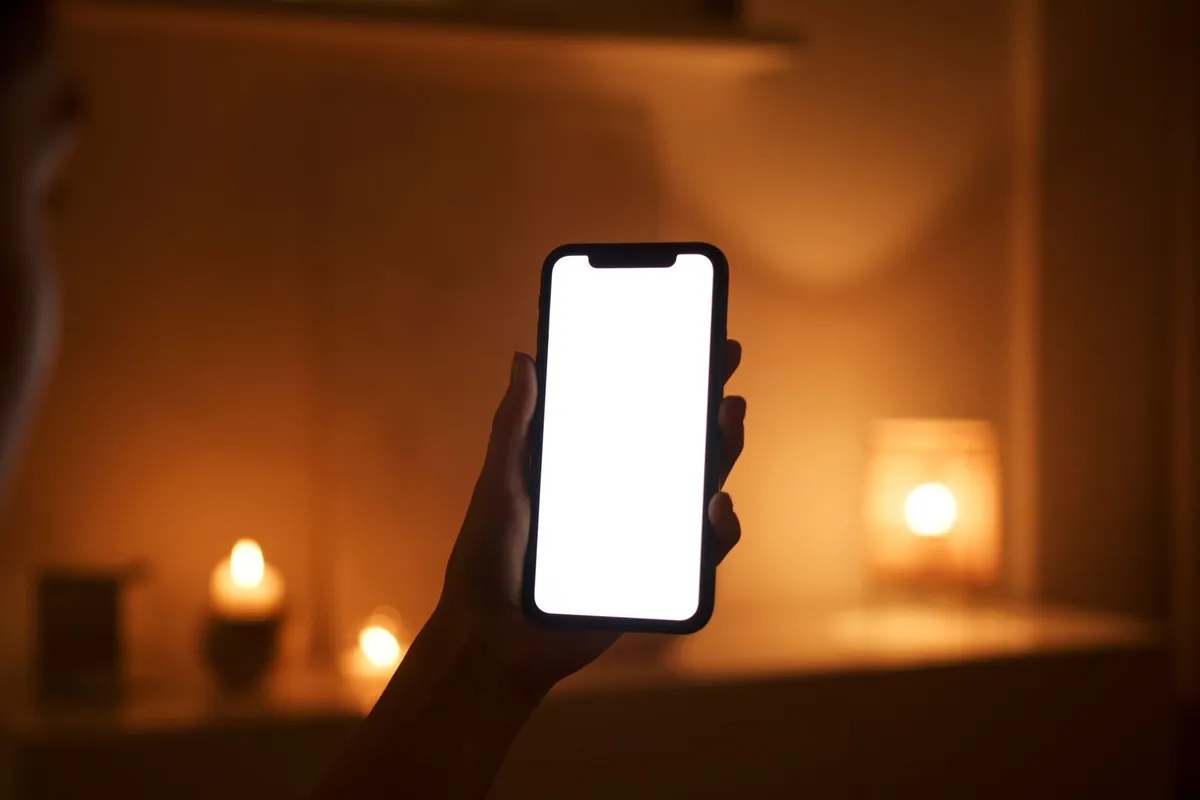 Hand hält ein Smartphone in einem warm beleuchteten Wohnzimmer mit Kerzen
