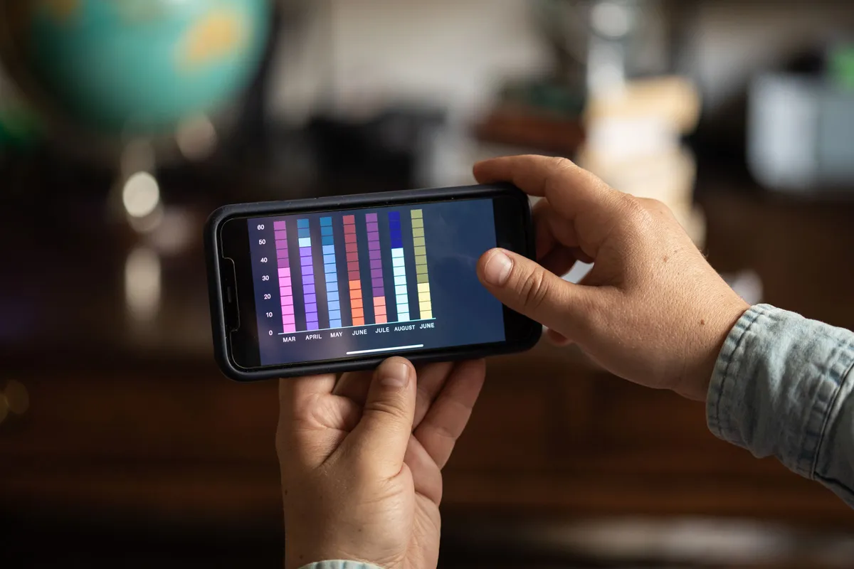 Hände halten ein Smartphone mit einem bunten Balkendiagramm