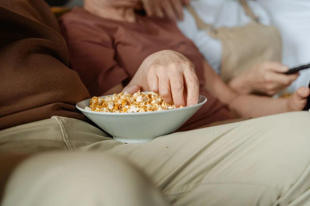 Schale mit Popcorn auf dem Schoß einer Person auf dem Sofa