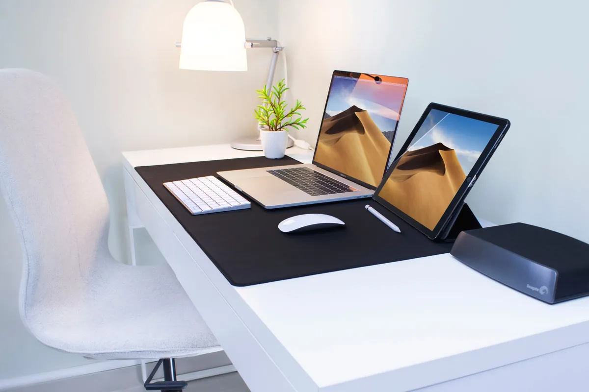 Laptop und Tablet auf einem weißen Schreibtisch mit Lampe und Pflanze