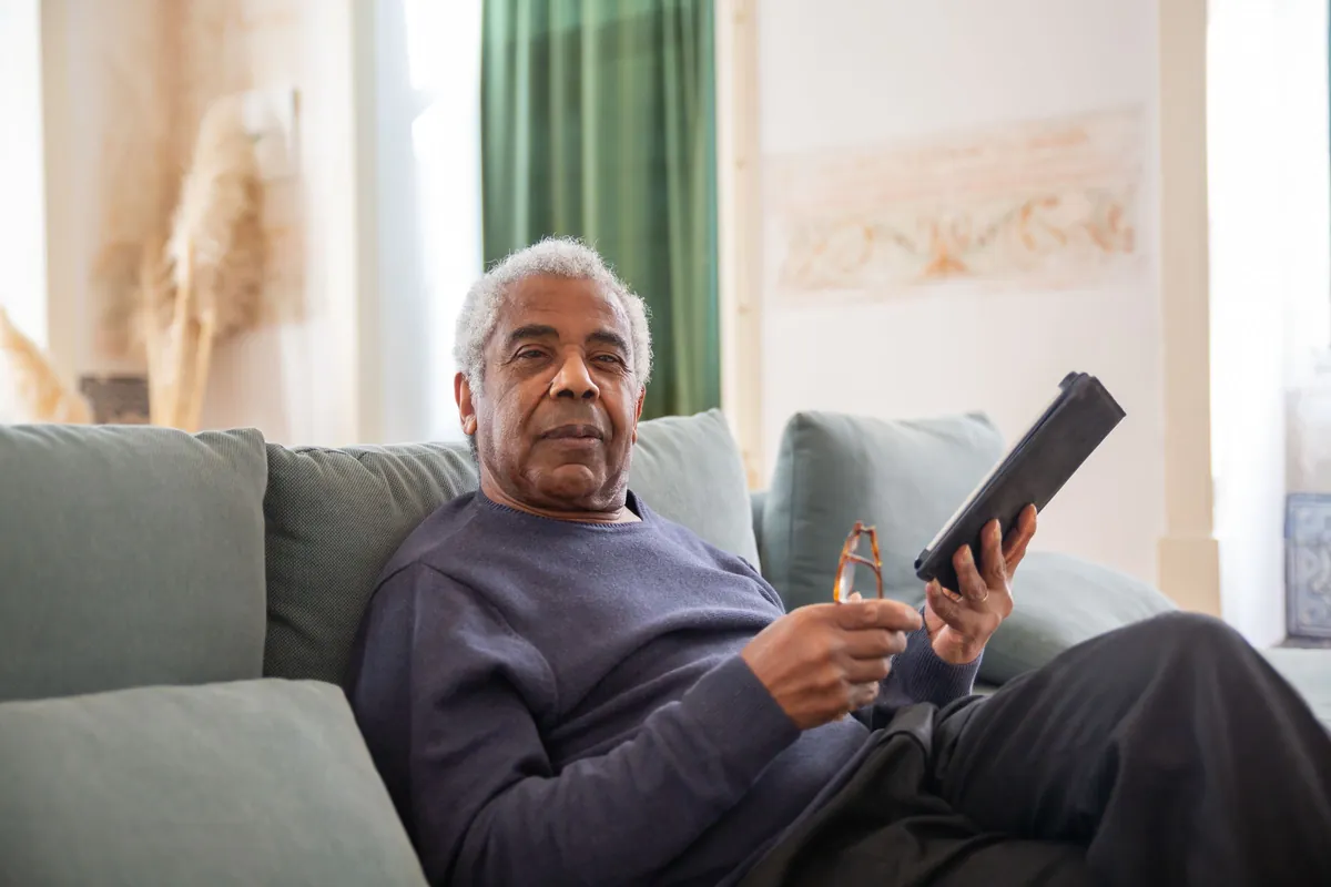 Älterer Mann sitzt auf dem Sofa und hält ein Tablet in der Hand