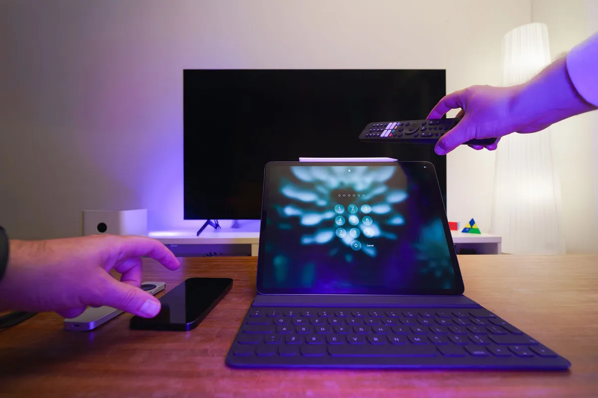 Tablet mit Tastatur vor einem Fernseher, eine Hand hält eine Fernbedienung