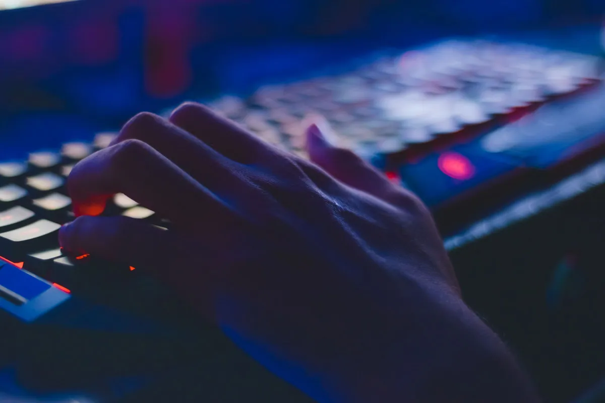 Hand auf einer beleuchteten Tastatur im Halbdunkel