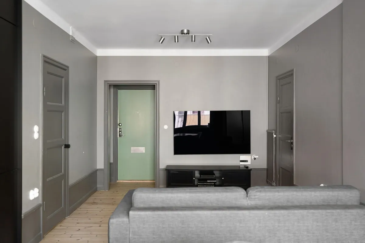 Schlichtes Wohnzimmer mit grauem Sofa und Wandfernseher über einem TV-Board