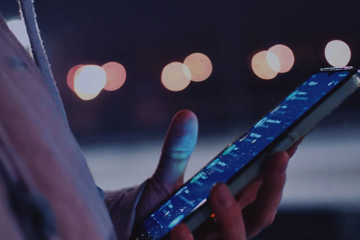 Hand hält am Abend ein Smartphone mit einer Liste auf dem Bildschirm