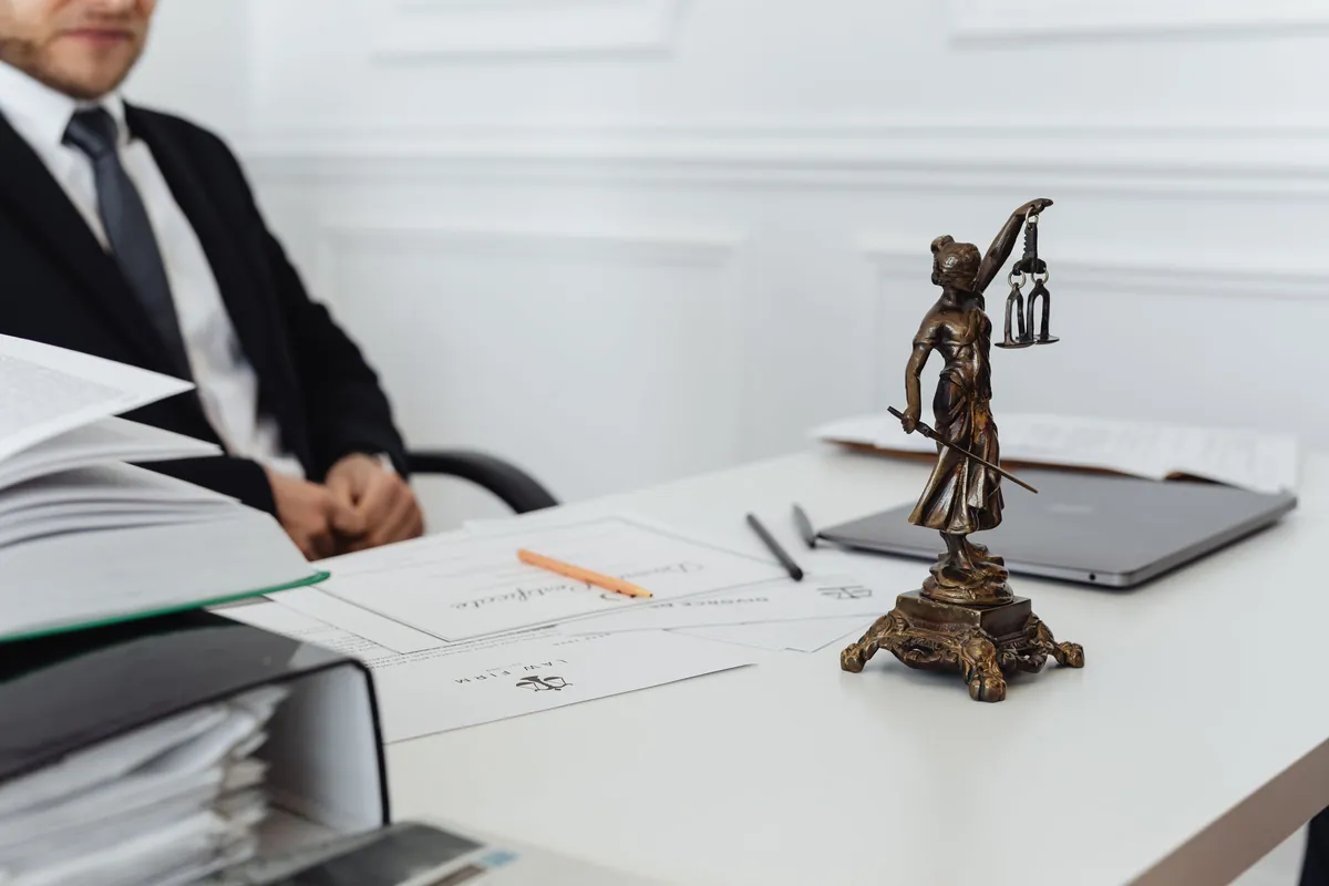 Schreibtisch in einer Kanzlei mit Justitia-Figur, Aktenordnern und Dokumenten