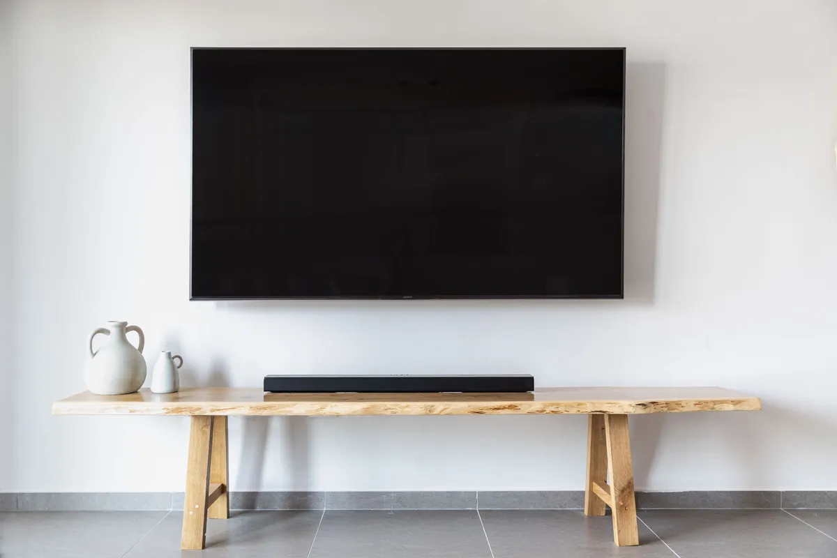 Flachbildfernseher an einer weißen Wand über einem Holz-Lowboard mit Soundbar