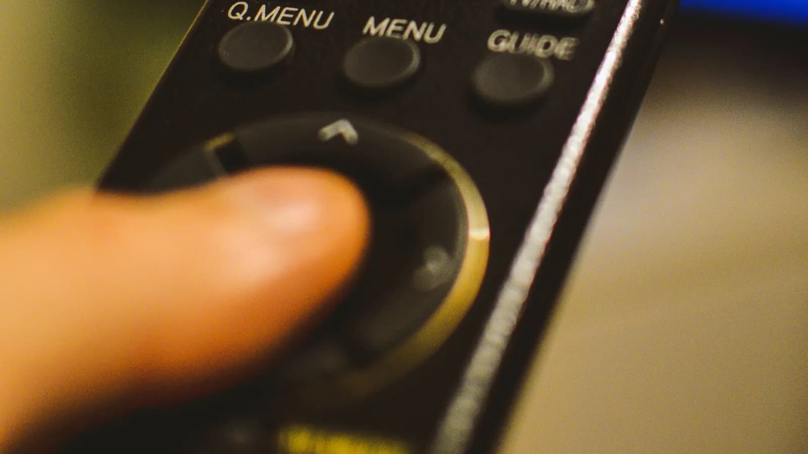 Daumen auf dem Navigationsring einer Fernbedienung mit Tasten für Menü und TV-Guide