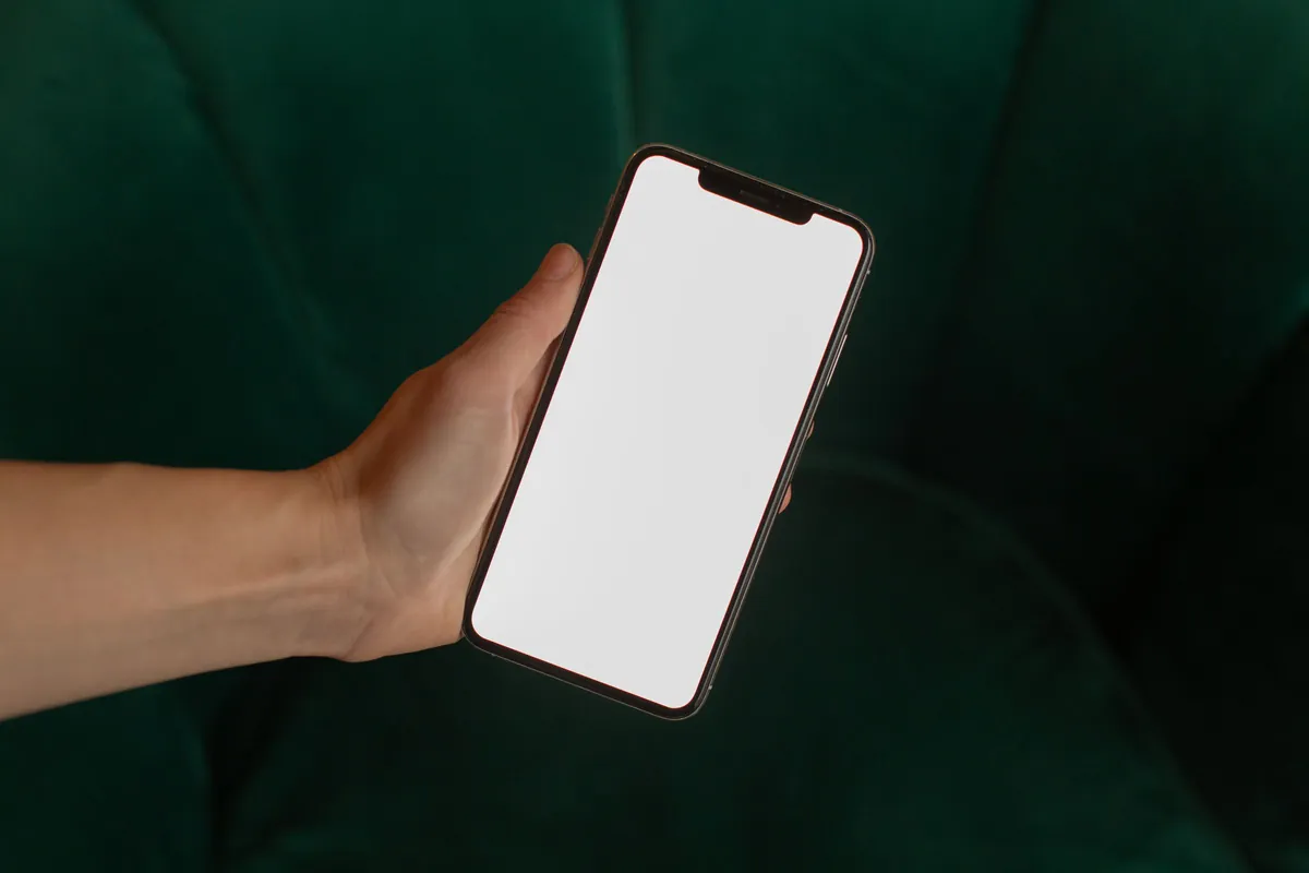 Hand hält ein Smartphone mit leerem Bildschirm vor dunkelgrünem Hintergrund