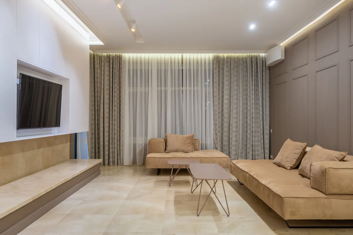 Großzügiges Wohnzimmer mit beigem Sofa und an der Wand montiertem Fernseher