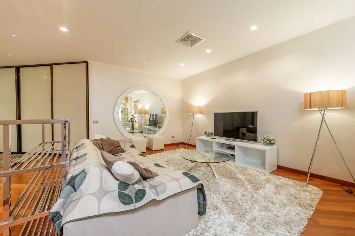 Helles Wohnzimmer mit Sofa, Stehlampe und Fernseher auf einem Lowboard