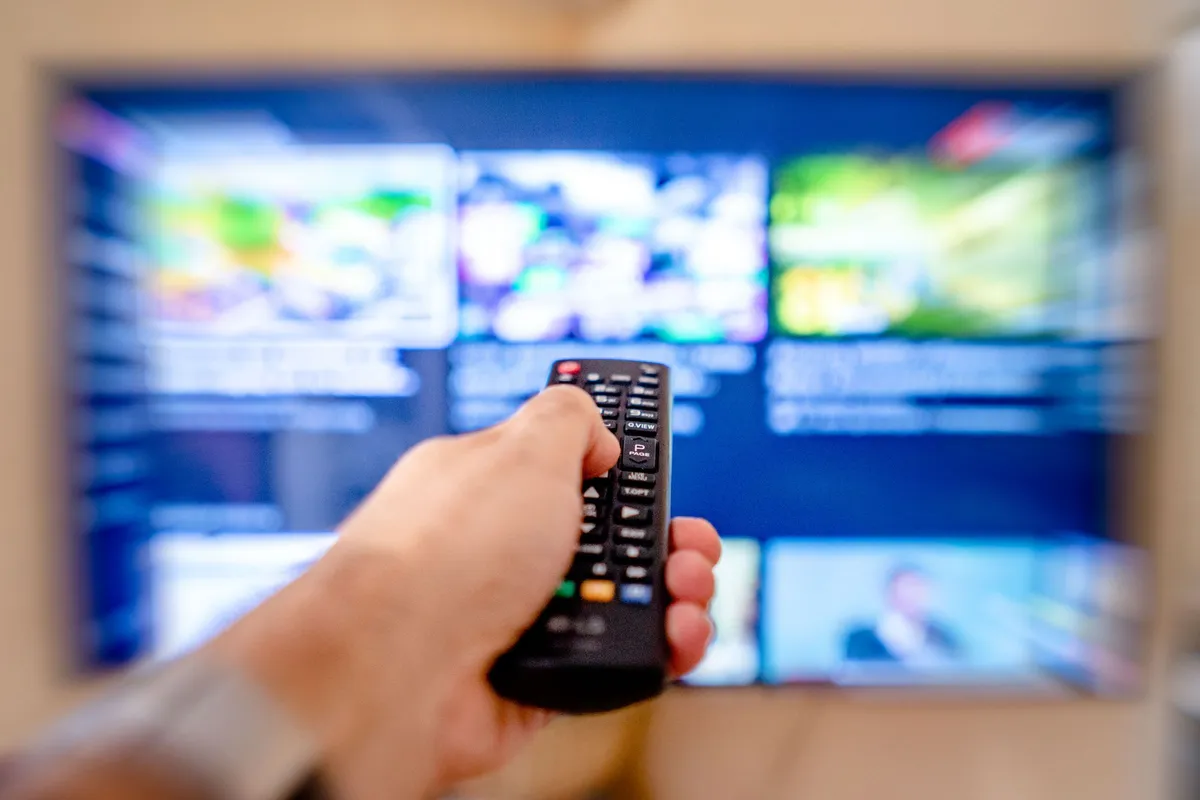 Hand richtet eine Fernbedienung auf einen Fernseher mit unscharfer App-Übersicht